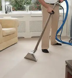 Professional carpet cleaner using a hot-water extraction wand and hose machine in a living room in Kansas City, MO.