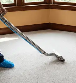 Steam carpet cleaning technician using a hot-water extraction wand on a residential carpet, wearing blue protective shoe covers Kansas City, MO.