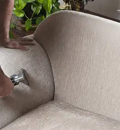 Professional upholstery cleaner deep-cleaning a fabric sofa with a handheld extraction tool and hose Kansas City, MO.