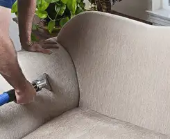 Professional upholstery cleaner deep-cleaning a fabric sofa with a handheld extraction tool and hose in Kansas City, MO.